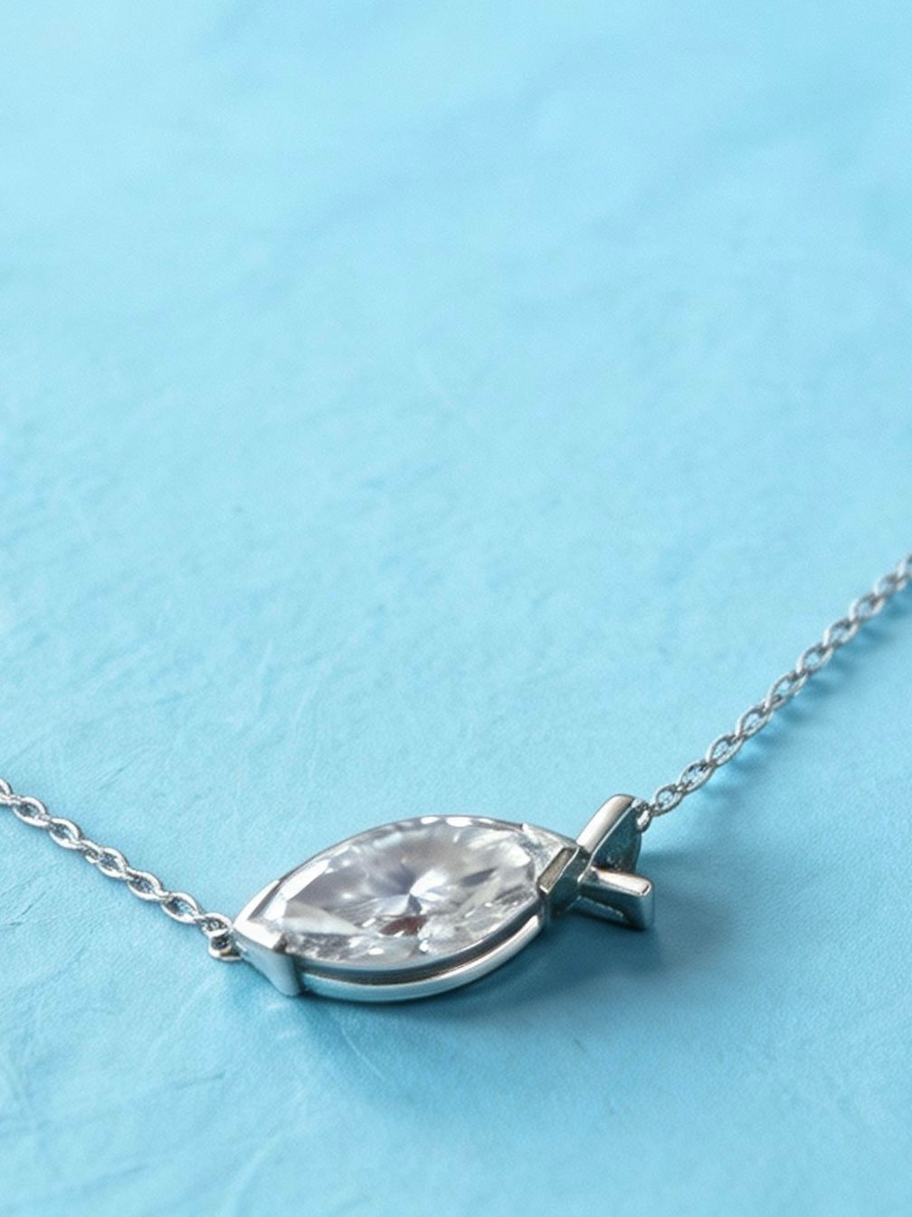 A silver east west marquise diamond pendant necklace, resting on a textured light blue surface.